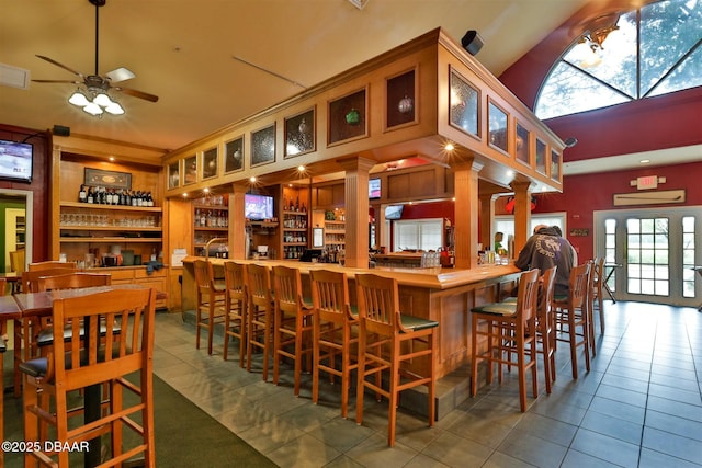 bar with tile patterned floors, ornate columns, a towering ceiling, and ceiling fan