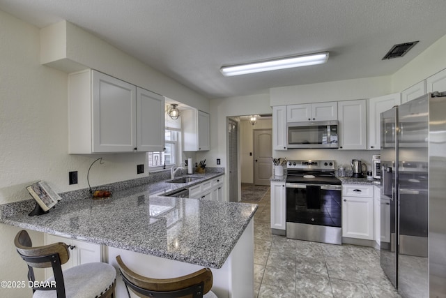 1408 Mollie Rd, Daytona Beach, FL 32114 - kitchen with stainless steel appliances, a peninsula, dark stone counters, a kitchen breakfast bar, and white cabinets