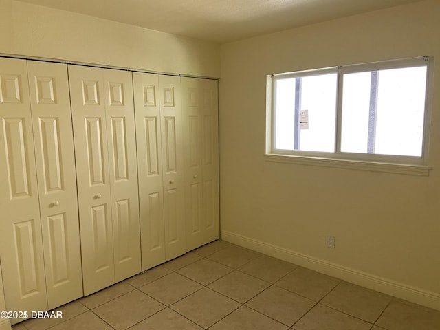 unfurnished bedroom with light tile patterned floors, a closet, and baseboards