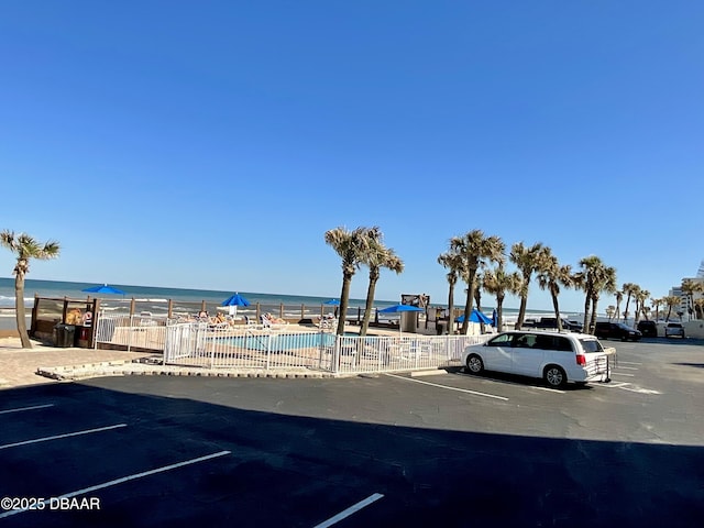 uncovered parking lot with a community pool, fence, and a water view