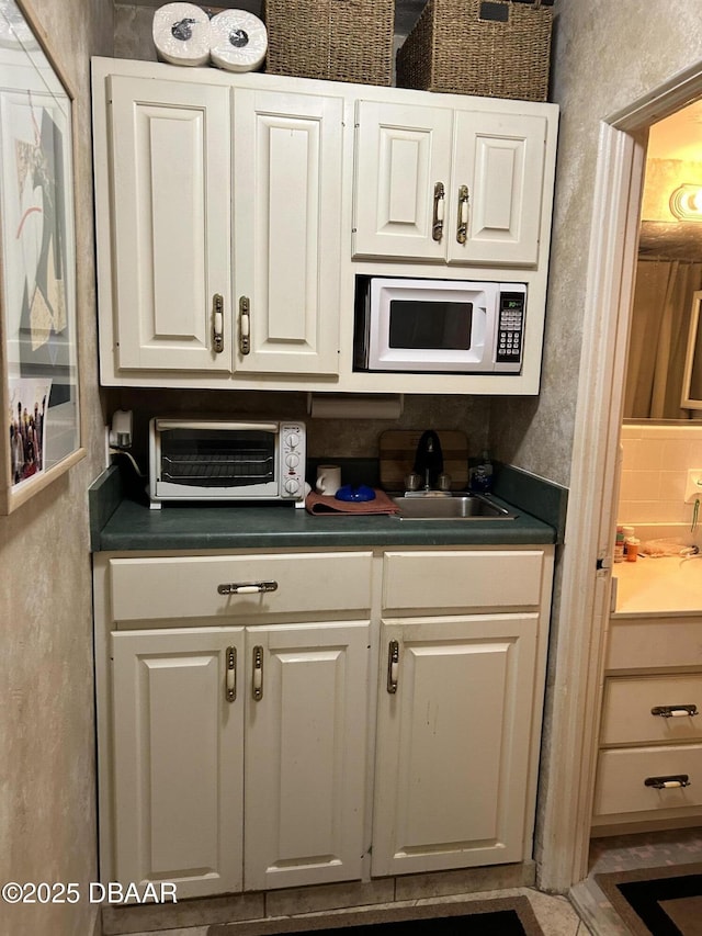 kitchen with white microwave, dark countertops, a toaster, white cabinetry, and a sink