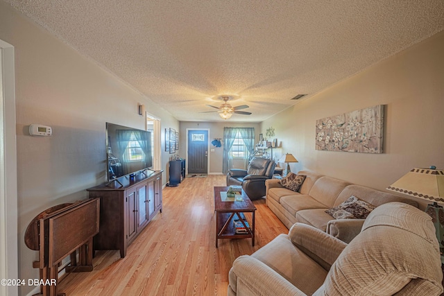 living room with light hardwood / wood-style floors, ceiling fan, and a textured ceiling