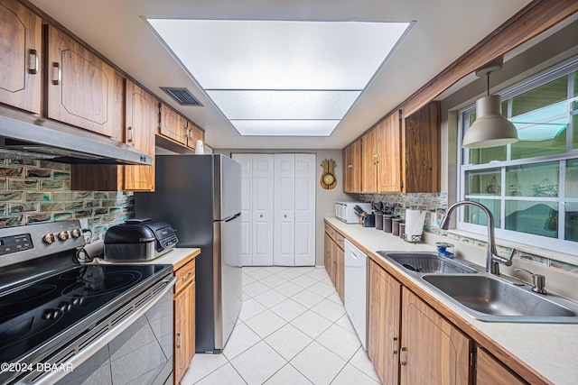 kitchen with stainless steel appliances, sink, light tile patterned floors, hanging light fixtures, and range hood