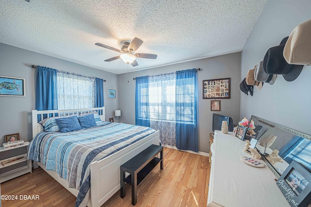 bedroom with a textured ceiling, wood-type flooring, multiple windows, and ceiling fan