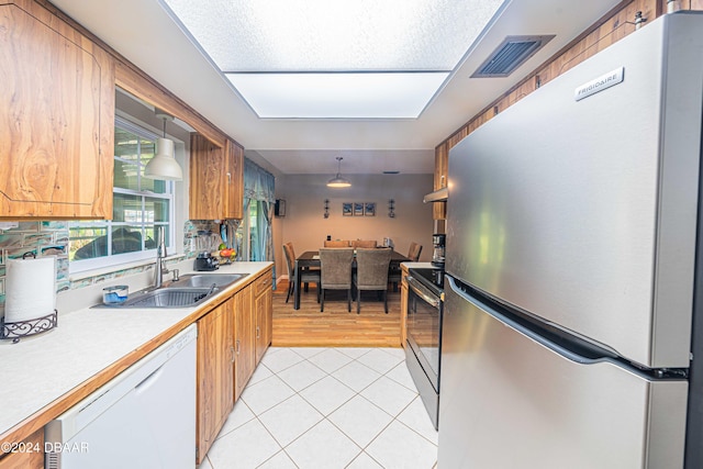 kitchen with light wood-type flooring, stainless steel refrigerator, hanging light fixtures, sink, and dishwasher