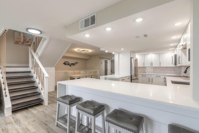 kitchen with a peninsula, a sink, visible vents, white cabinetry, and light countertops