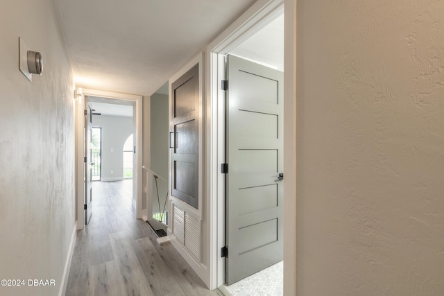 hall with baseboards, a textured wall, and light wood-style floors