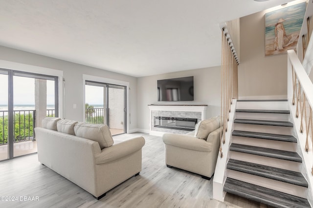 living room featuring light wood-style flooring, stairway, baseboards, and a glass covered fireplace