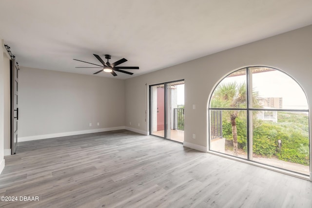 empty room with ceiling fan, a barn door, baseboards, and light wood-style floors