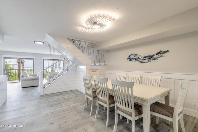 dining room featuring light wood finished floors, stairway, a decorative wall, and a wainscoted wall