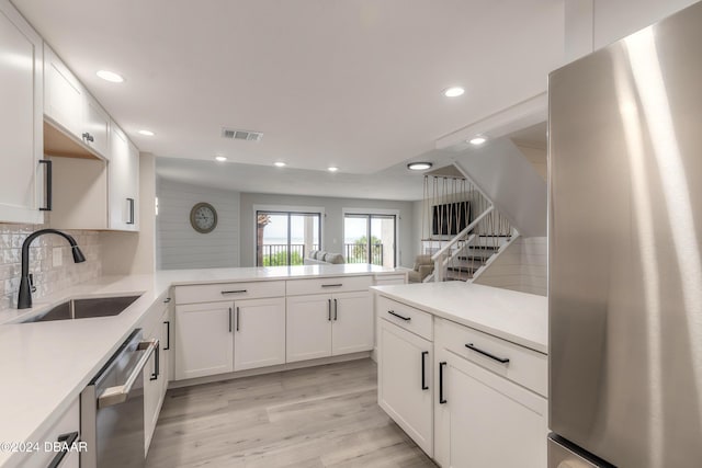 kitchen with a peninsula, stainless steel appliances, light countertops, white cabinetry, and a sink