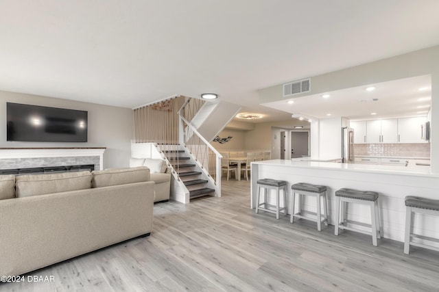 living area with recessed lighting, visible vents, stairway, a stone fireplace, and light wood-type flooring