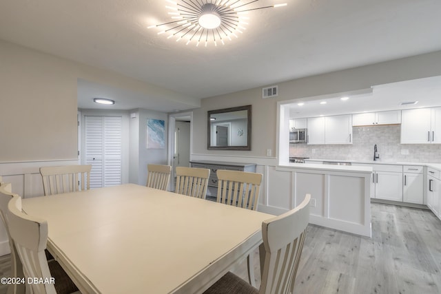 dining space with a wainscoted wall, light wood-style flooring, visible vents, and a decorative wall