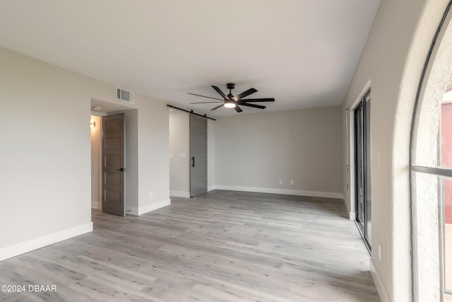 spare room featuring light wood-type flooring, a barn door, visible vents, and ceiling fan