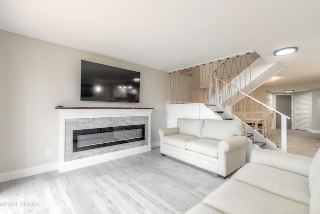 unfurnished living room featuring light wood finished floors, baseboards, stairway, and a glass covered fireplace