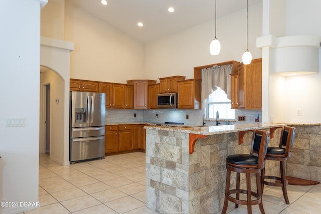 kitchen featuring light stone countertops, high vaulted ceiling, kitchen peninsula, a breakfast bar, and appliances with stainless steel finishes