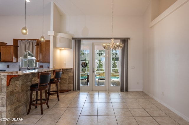 kitchen with light tile patterned floors, a towering ceiling, light stone counters, and pendant lighting