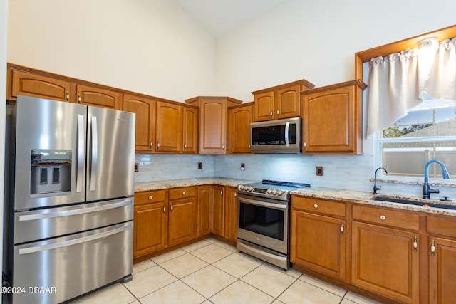 kitchen featuring light stone countertops, stainless steel appliances, sink, light tile patterned floors, and high vaulted ceiling