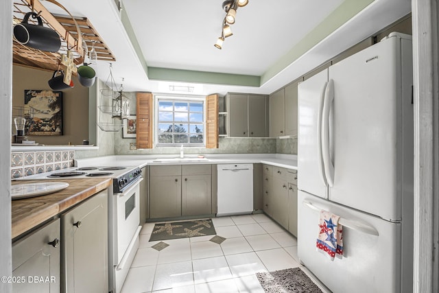 kitchen with sink, light tile patterned floors, gray cabinets, white appliances, and decorative backsplash