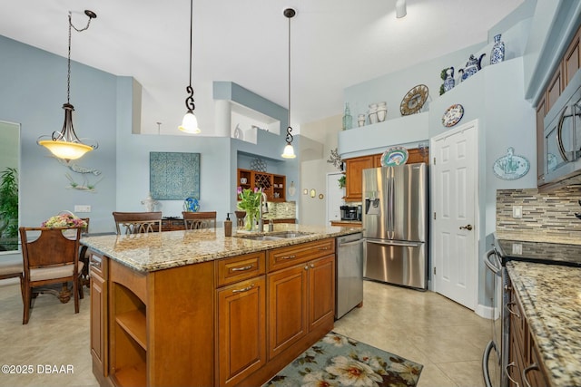 kitchen with appliances with stainless steel finishes, decorative light fixtures, an island with sink, sink, and light stone counters