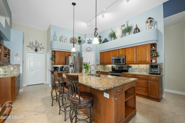 kitchen featuring sink, appliances with stainless steel finishes, hanging light fixtures, light stone counters, and an island with sink