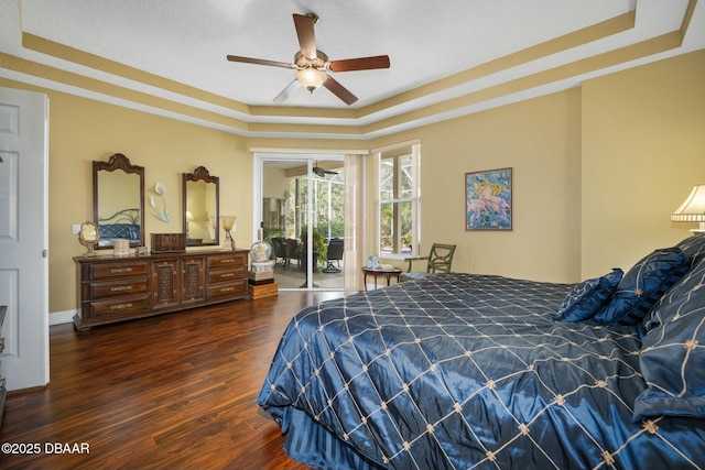 bedroom with dark hardwood / wood-style floors, access to outside, a raised ceiling, and ceiling fan