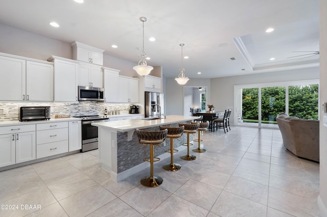 kitchen featuring a breakfast bar area, a kitchen island with sink, white cabinetry, appliances with stainless steel finishes, and decorative light fixtures