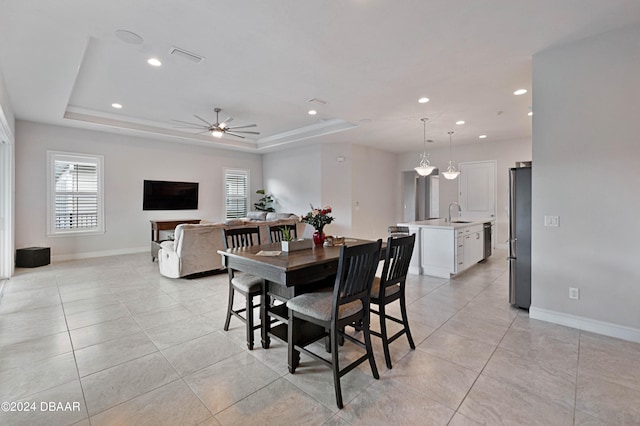 tiled dining area with ceiling fan, a raised ceiling, and sink