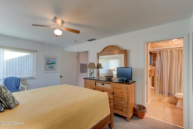 carpeted bedroom featuring multiple windows, visible vents, a textured ceiling, and ensuite bathroom