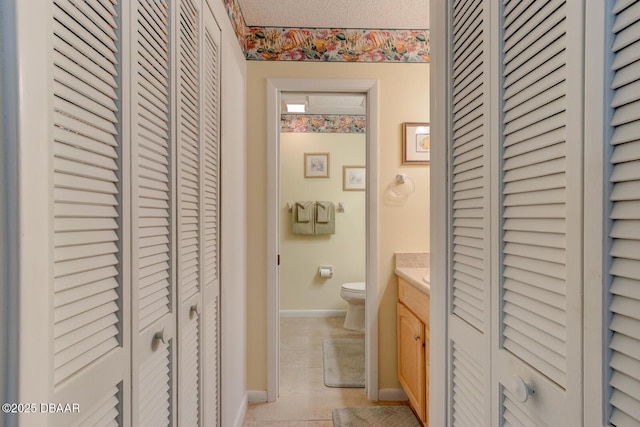 bathroom with a textured ceiling, toilet, vanity, baseboards, and a closet