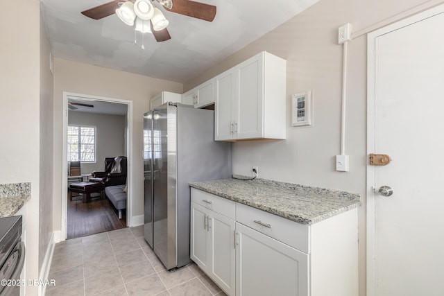 kitchen with light tile patterned floors, ceiling fan, white cabinets, freestanding refrigerator, and light stone countertops