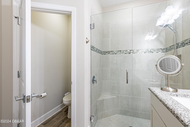 bathroom featuring hardwood / wood-style flooring, a shower with shower door, vanity, and toilet