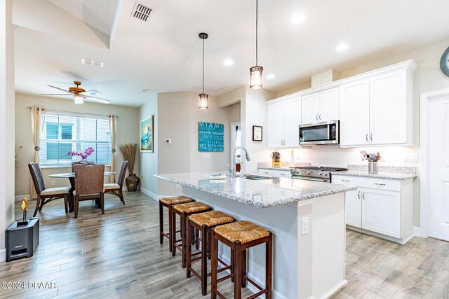 kitchen featuring light hardwood / wood-style floors, white cabinetry, sink, appliances with stainless steel finishes, and a kitchen island with sink