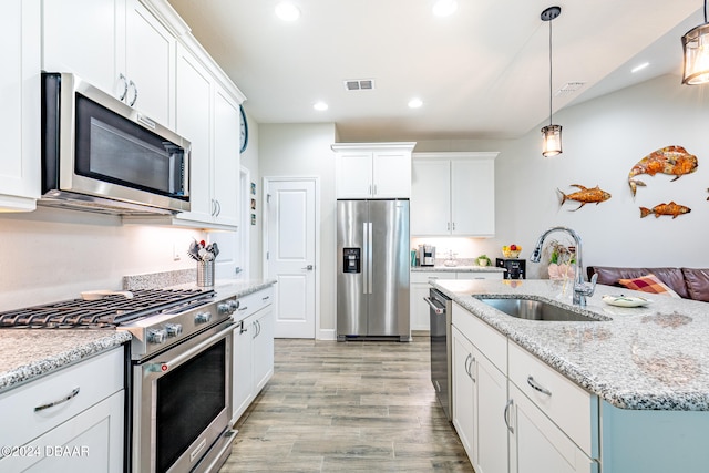 kitchen featuring white cabinetry, sink, appliances with stainless steel finishes, decorative light fixtures, and light wood-type flooring