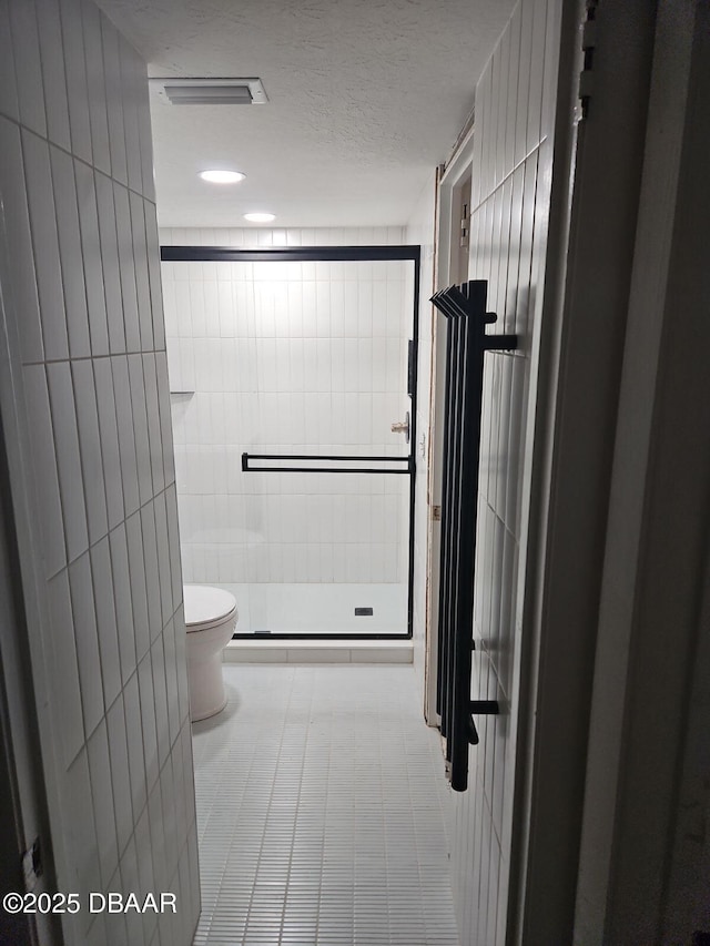 full bathroom featuring visible vents, a shower stall, a textured ceiling, tile walls, and toilet