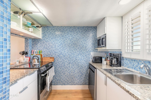 kitchen with light wood finished floors, a sink, white cabinetry, appliances with stainless steel finishes, and light countertops