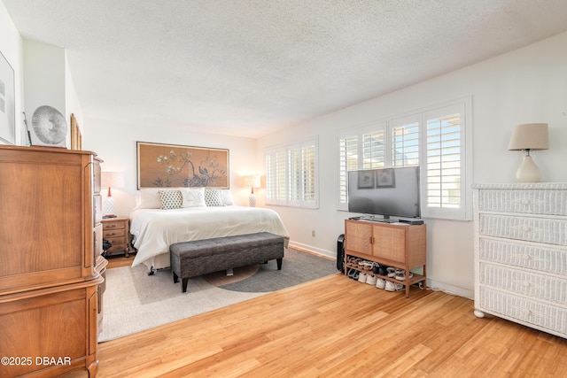 bedroom with baseboards, light wood finished floors, and a textured ceiling