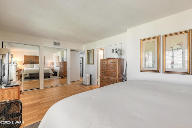 bedroom with a textured ceiling, multiple closets, visible vents, and light wood-type flooring