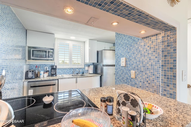 kitchen with backsplash, light stone counters, stainless steel appliances, white cabinetry, and a sink