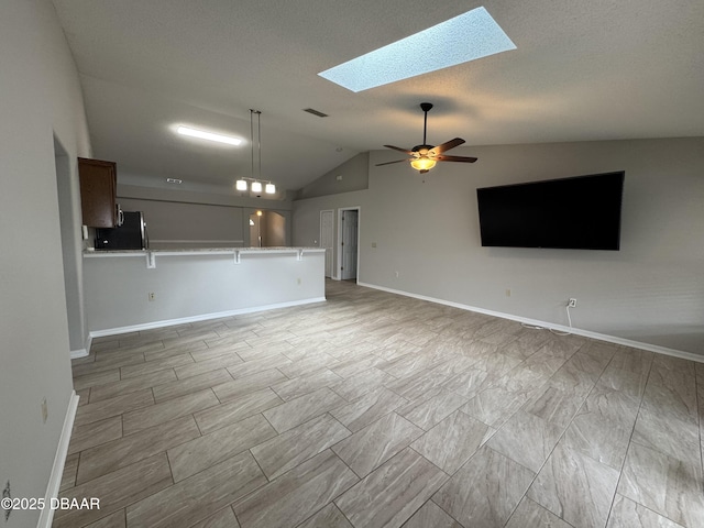 unfurnished living room featuring vaulted ceiling with skylight and ceiling fan