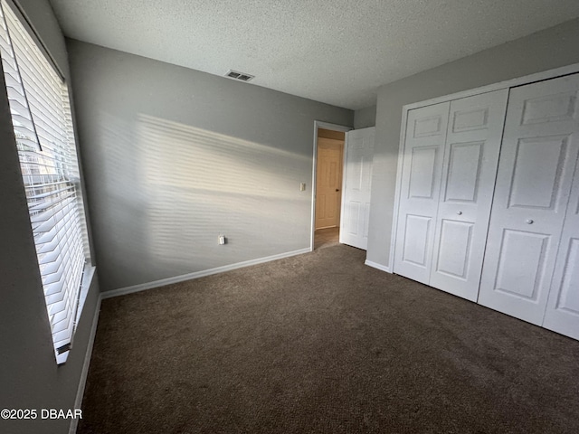 unfurnished bedroom with dark carpet, a closet, and a textured ceiling