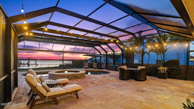 patio terrace at dusk featuring a water view, a pool with hot tub, and a lanai