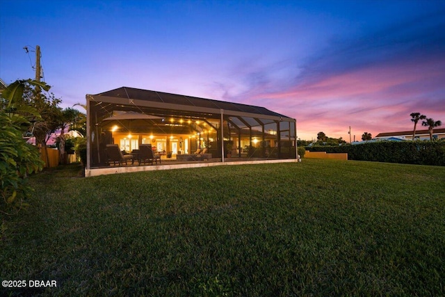 back house at dusk with a yard, a patio area, and glass enclosure