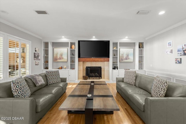 living room with ornamental molding, built in features, and light hardwood / wood-style flooring