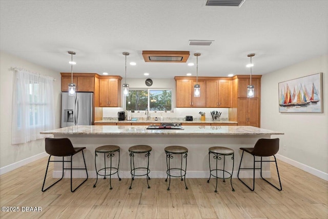 kitchen featuring stainless steel refrigerator with ice dispenser, a kitchen breakfast bar, a spacious island, and pendant lighting