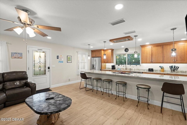 kitchen featuring light hardwood / wood-style floors, stainless steel refrigerator with ice dispenser, a kitchen bar, hanging light fixtures, and light stone counters