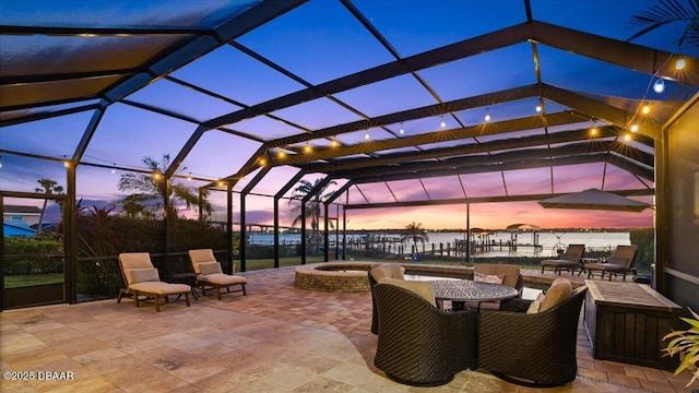 patio terrace at dusk featuring glass enclosure, a water view, and an in ground hot tub