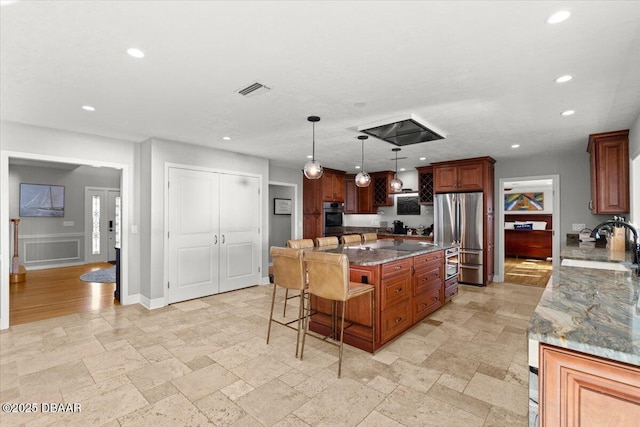 kitchen featuring pendant lighting, a kitchen island, dark stone countertops, a kitchen breakfast bar, and stainless steel fridge