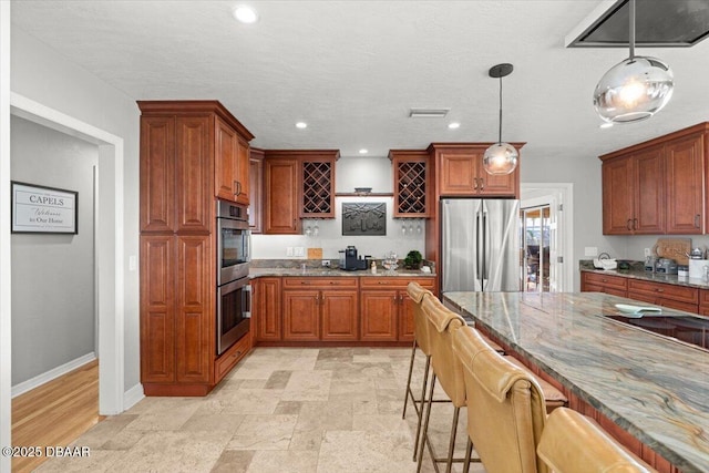 kitchen with appliances with stainless steel finishes, pendant lighting, a kitchen bar, and dark stone counters