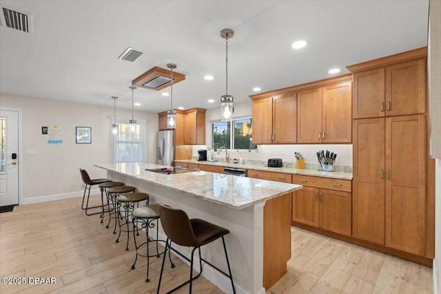 kitchen with appliances with stainless steel finishes, pendant lighting, light stone counters, a breakfast bar, and a center island